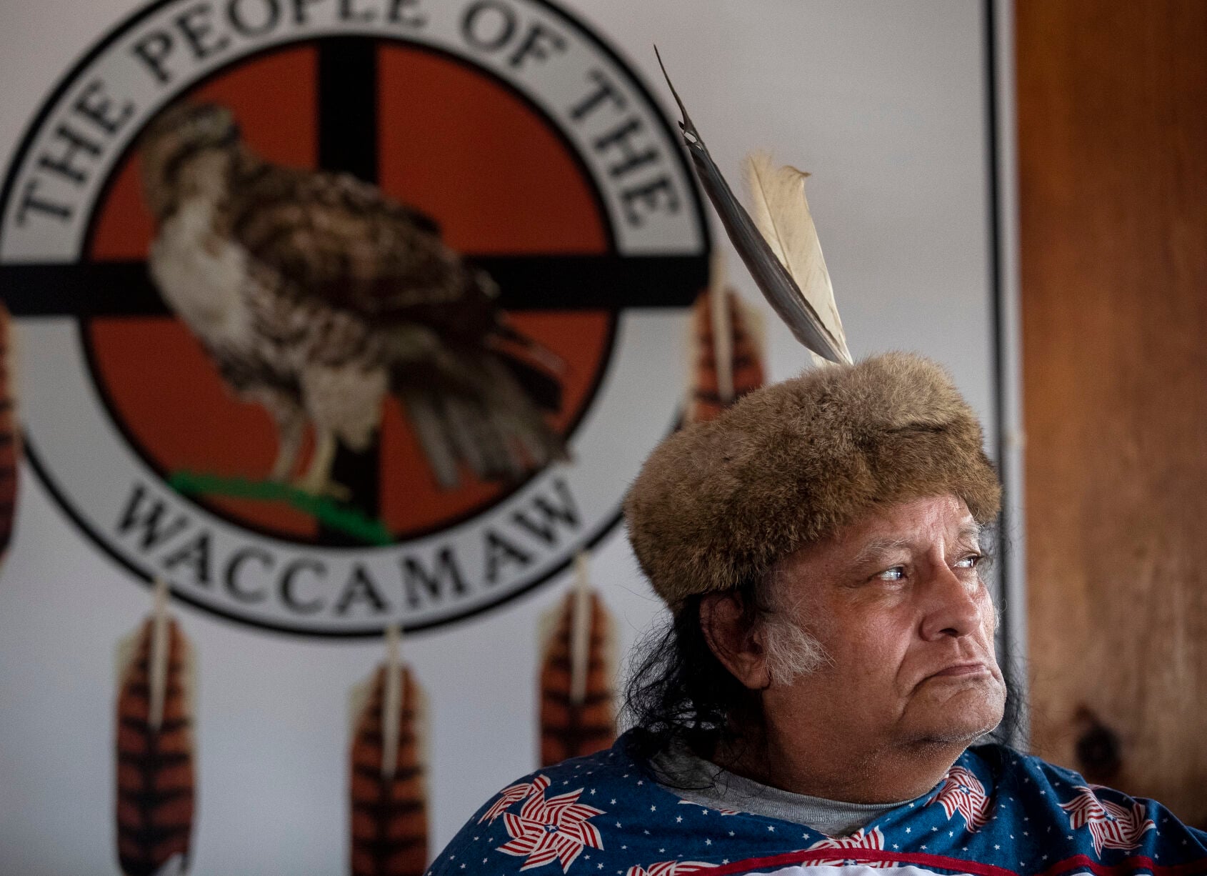 Chief Harold 'Buster' Hatcher before the seal of the People of the Waccamaw, in a fur turban and eagle feather
