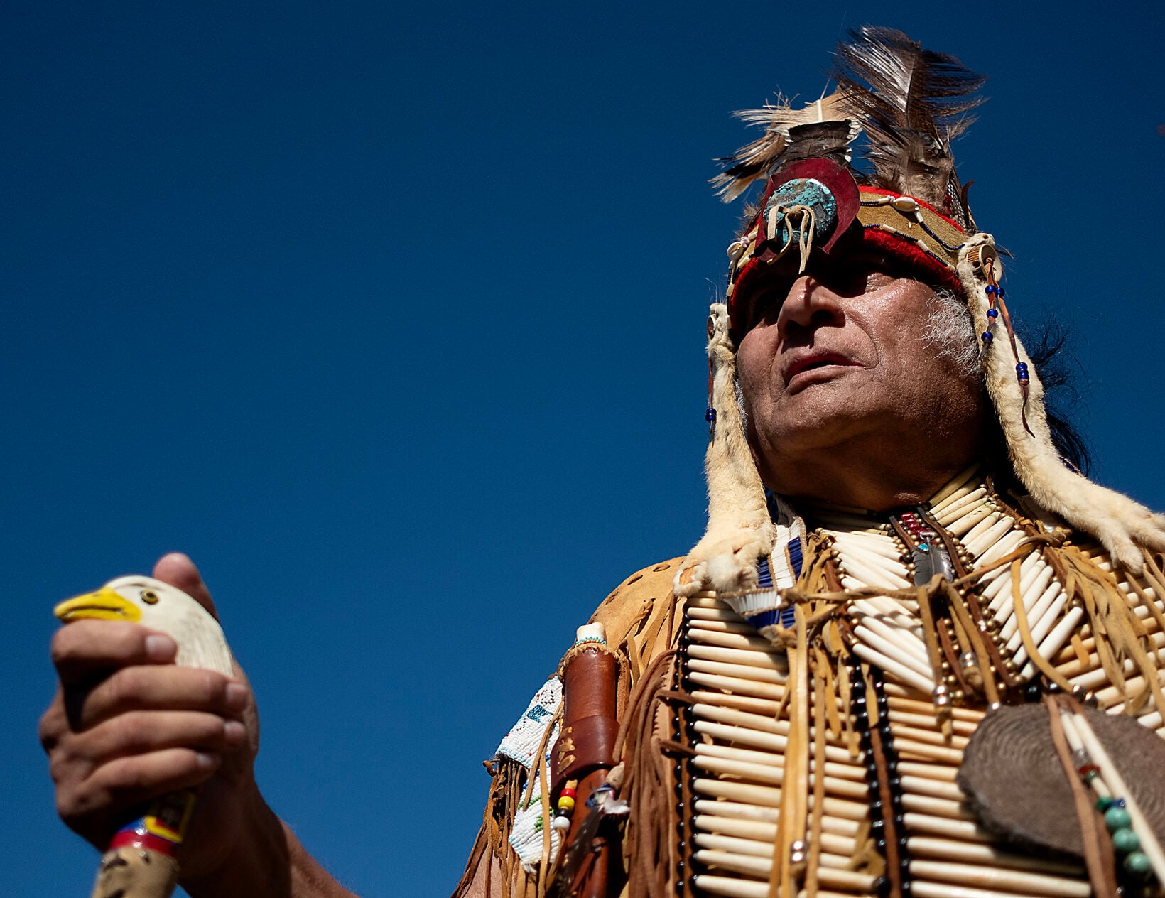 Chief Harold 'Buster' Hatcher in full regalia against the sky, eagle-head staff in hand