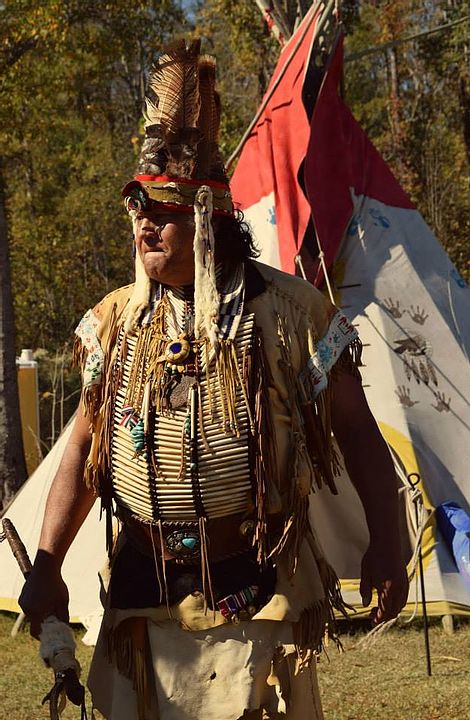 In full regalia — breastplate and headdress — before the tipis at a Waccamaw gathering